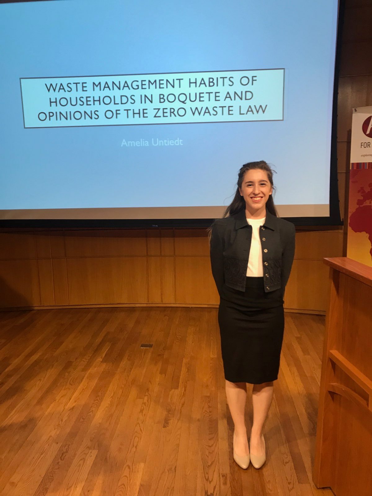 A woman smiling in front of a screen that says Waste management habits of households in Boquete and opinions of zero waste law